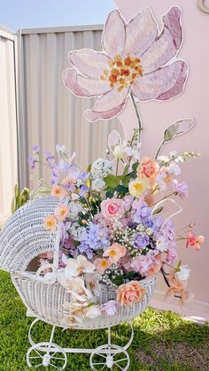 a basket filled with lots of flowers sitting on top of a grass covered field next to a fence