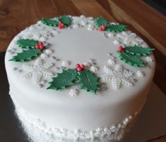 a white frosted cake decorated with holly leaves and red berries on a wooden table