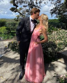 a man in a tuxedo kissing a woman in a pink dress under a tree