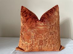 an orange velvet pillow sitting on top of a white bed sheet covered in brown fabric