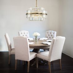 a chandelier hangs above a round dining table with white upholstered chairs