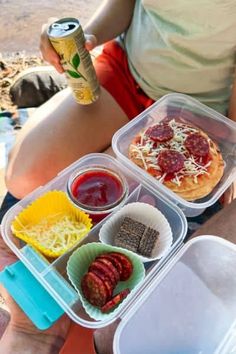 a woman sitting on the beach with some food in her lap and a can of soda