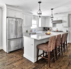 a kitchen with white cabinets and an island that has four bar stools in front of it