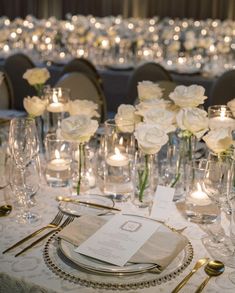 the table is set with silverware and white roses in vases, candles and napkins