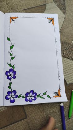 an open notebook with blue flowers on it and a green pen in the corner next to it