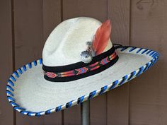 You will be styling in this colorful Gus palm hat. It's a flattering hat that has been hand laced in black and cobalt blue. Black suede serves as the base for the beaded hatband. The back of the band has a deer antler bead. The finishing details include an antique silver Concho and a feather of orange and blue that pull all the colors together.It has a 4" brim and 5 1/4" crown. Each hat is made to order. Please allow up to 4 weeks for your hat to ship. Traditional Fitted Blue Hat, Adjustable Blue Fedora For Western-themed Events, Blue Adjustable Custom Hat Bands, Custom Adjustable Summer Hat Bands, Southwestern Blue Hat With Curved Brim, Southwestern Style Blue Hat With Curved Brim, Artisan Blue Hat Bands For Country Events, Southwestern Style Adjustable Fedora For Kentucky Derby, Traditional Summer Hat Bands For Rodeo