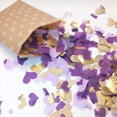 purple and gold confetti spilling out of a brown paper bag on a white surface