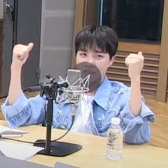 a person sitting at a table with a microphone in front of him and giving the thumbs up sign