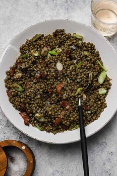 a white bowl filled with lentils next to a glass of water