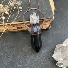 This necklace has been made with a polished black obsidian crystal point topped with mini quartz crystals and adorned with a rainbow moonstone. It is set with electroformed copper and has been oxidized for an antique finish. The pendant measures just over 2 1/2 inches long. It will come on a 24 inch chain in your choice of gunmetal or dark copper(shown in photo). Just let me know if you would like your chain length customized at no extra cost. All metals used in my items are lead/nickel free. About electroforming: I make my jewelry pieces using a process called Electroforming, which uses electricity to fuse copper onto other objects. If you'd like to see how they are made, you can view my process video here: https://www.youtube.com/watch?v=NFjTOr65oWc&t=75s All orders come in a gift box pa Mystical Handmade Black Crystal Necklaces, Handmade Mystical Black Crystal Necklace, Handmade Black Mystical Crystal Necklace, Black Labradorite Spiritual Necklaces, Black Moonstone Spiritual Jewelry, Spiritual Black Moonstone Jewelry, Black Moonstone Necklace For Gift, Black Labradorite Pendant Necklace, Black Obsidian Crystal