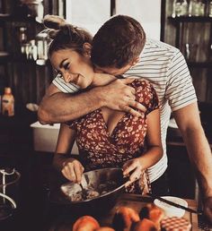 a man hugging a woman in the kitchen while she is mixing something into a bowl