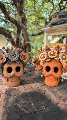 two skulls with flowers on their heads sitting next to each other in front of a tree