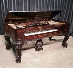 an old piano sitting on top of a carpeted floor next to a black curtain