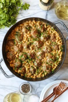 a pan filled with pasta and meatballs on top of a marble table next to wine glasses