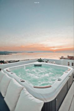 a hot tub sitting on top of a wooden deck next to the ocean at sunset