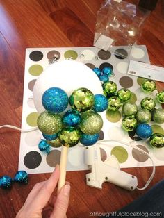 a person is decorating christmas balls with green and blue ornaments on a polka dot table