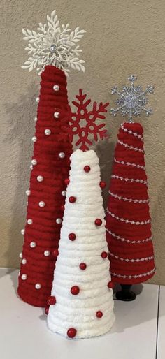 three knitted christmas trees sitting on top of a white table next to snowflakes