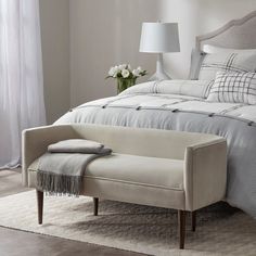 a bed with a white comforter and pillows on top of it next to a lamp