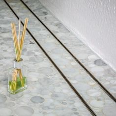 two reeds in a small glass vase on a tiled floor next to a wall