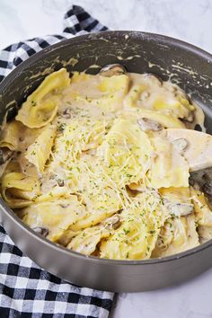 a pan filled with pasta and mushrooms on top of a checkered table cloth next to a wooden spoon