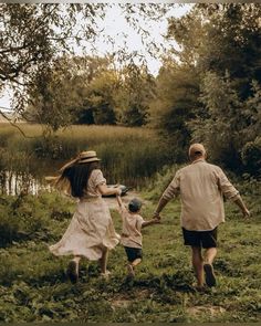 a man and woman holding hands as they walk through the grass with a child in their arms