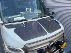 an electric vehicle parked in front of a garage door with the hood up and engine out