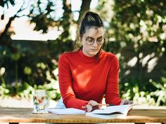 a woman sitting at a table with a book and pen in her hand while writing