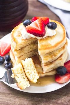 a stack of pancakes with strawberries and blueberries cut in half on a white plate