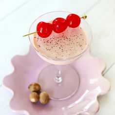 a drink with cherries in it sitting on a pink plate next to some nuts