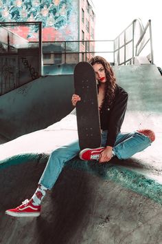 a woman sitting on the edge of a skateboard ramp holding up her skateboard