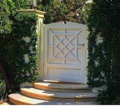 a white gate with steps leading up to it in front of some trees and bushes