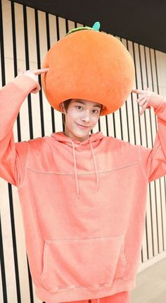 a young man wearing an orange hat on top of his head while standing in front of a wall