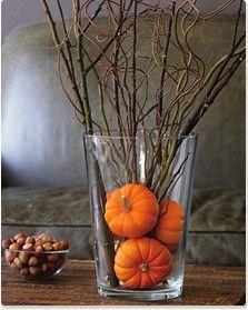 a vase filled with branches and orange pumpkins