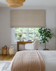 a white bed sitting under a window next to a wooden desk and chair in a bedroom