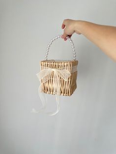 a hand holding a small basket with a bow on the handle and pearls hanging from it