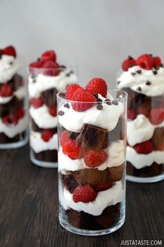 some desserts are in a glass on a table with raspberries and whipped cream