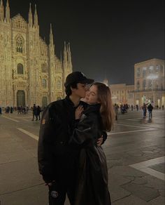 a man and woman kissing in front of a cathedral