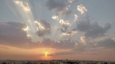 the sun is setting over a city with tall buildings in the foreground and clouds in the background