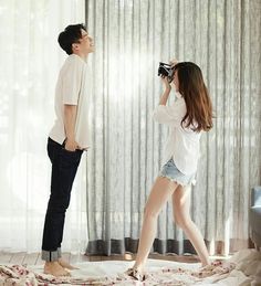 a man standing next to a woman on top of a bed in front of a window