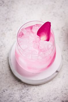 a pink drink with ice and a flower on the rim is sitting on a white plate