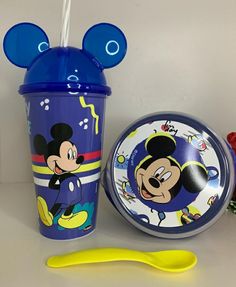 a mickey mouse sippy cup next to a yellow spoon