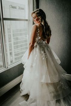 a woman standing in front of a window wearing a wedding dress