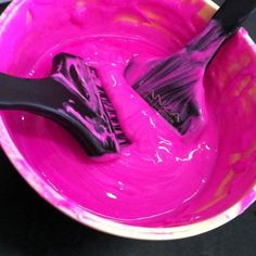 two black brushes in a pink bowl with purple paint on the inside and one brush sticking out of it