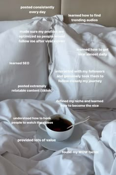 a cup of coffee sitting on top of a white bed covered in sheets and pillows