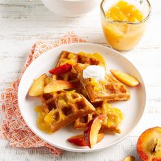 a white plate topped with waffles and fruit next to a glass of orange juice