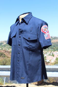 Check out this 4.1 ARC rated Industrial Safety Fire Protection short sleeve shirt. This is a must have for either working around fire or for a costume. Grab this piece today!  42 medium 4.1 ARC rated Dimensions Pit to pit:24"(58cm) Back:32"(81cm) Shoulder:19"(48cm) Sleeve:10"(25cm) 100 Cotton with Fire Retardant Coating Condition: Excellent, Used - This item appears to have had very little wear. No noticeable flaws or defects. If you have any questions about this item, please do not hesitate to ask. Thanks! westvalleywardrobe.com westvalleyforge.etsy.com email: westvalleyforge(at)gmail.com Instagram, Facebook & Twitter: @westvalleyforge Wardrobe and Stylists - We provide rentals to wardrobe and stylists. Please contact us for rental rates and special pricing at westvalleyforge(at)gmail.com Fitted Collared T-shirt With Pockets, Navy Fitted Short Sleeve T-shirt, Fitted Short Sleeve Shirt With Pockets, Cotton Short Sleeve Uniform Tops, Uniform Style Cotton Tops With Short Sleeves, Cotton Uniform Tops With Short Sleeves, Fitted Streetwear Shirt With Pockets, Navy Short Sleeve Shirt For Streetwear, Fitted Shirt With Pockets For Streetwear