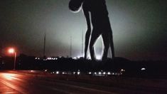 a silhouette of a man holding a basketball on the side of a road at night