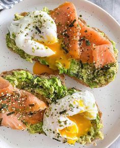 two pieces of toast with eggs, avocado and salmon on them sitting on a white plate