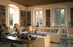 a living room filled with lots of furniture and bookshelves next to two windows