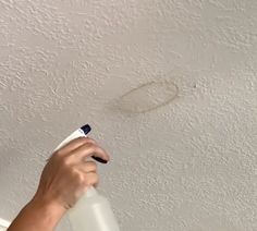 a person spraying paint on the ceiling with a sprayer and a white wall behind them